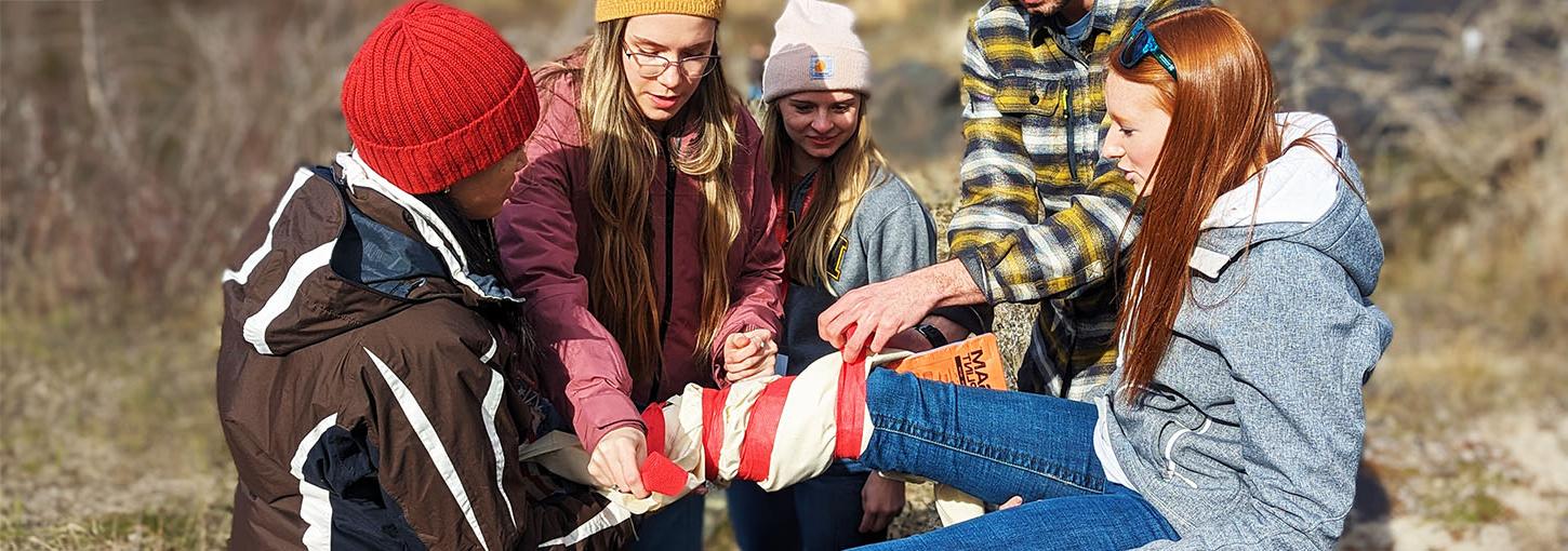 爱达荷州WWAMI students tie a leg brace around a volunteer victim during a medical simulation.